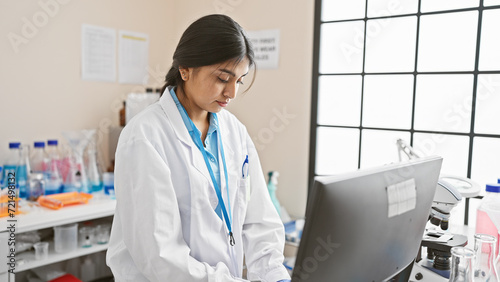 A focused indian woman scientist analyzes data on a computer in a laboratory setting  showcasing her professionalism.