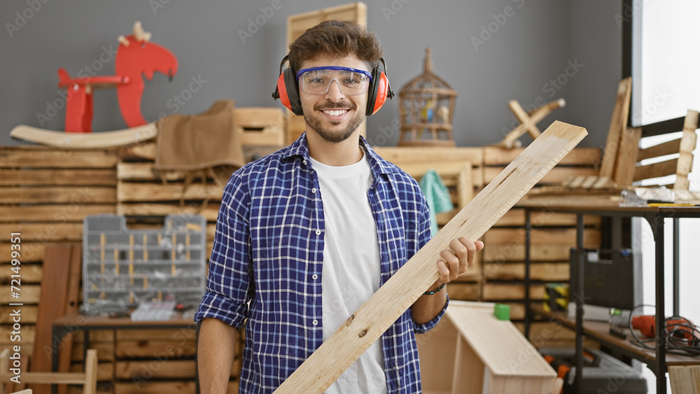 Handsome young arabian man with a beard, happily smiling as he carries a wood plank in his carpentry workshop, exuding confidence in his woodworking profession Handsome young arabian man with a beard, happily smiling as he carries a wood plank in his carpentry workshop, exuding confidence in his woodworking profession