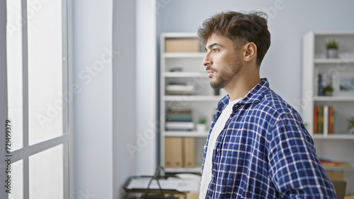 Young and successful arabic business worker, relaxed indoor looking through his office window, engrossed in deep thought while dealing with a serious issue at hand.