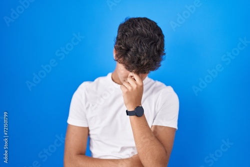 Hispanic teenager standing over blue background tired rubbing nose and eyes feeling fatigue and headache. stress and frustration concept.