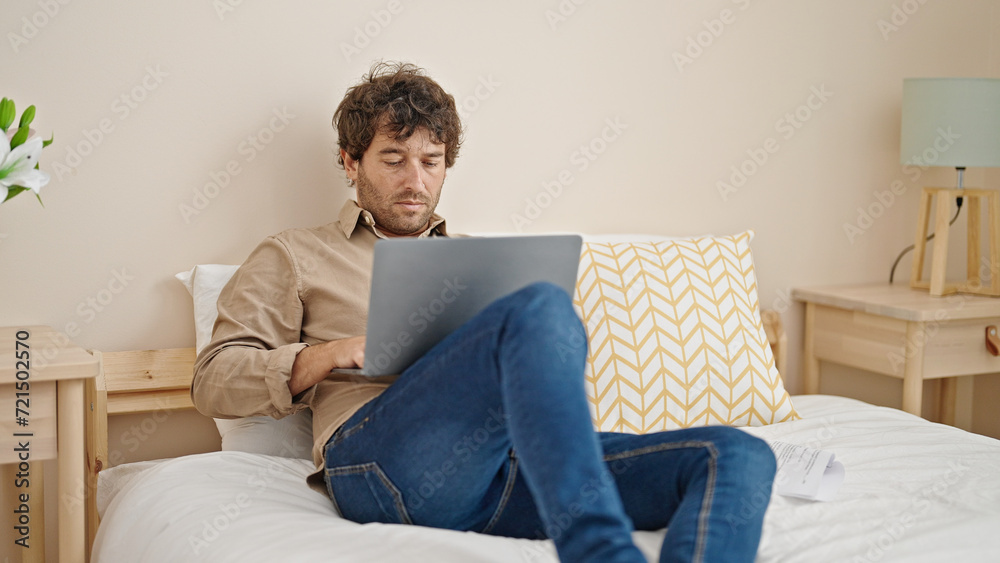 Young hispanic man using laptop sitting on bed at bedroom Young hispanic man using laptop sitting on bed at bedroom