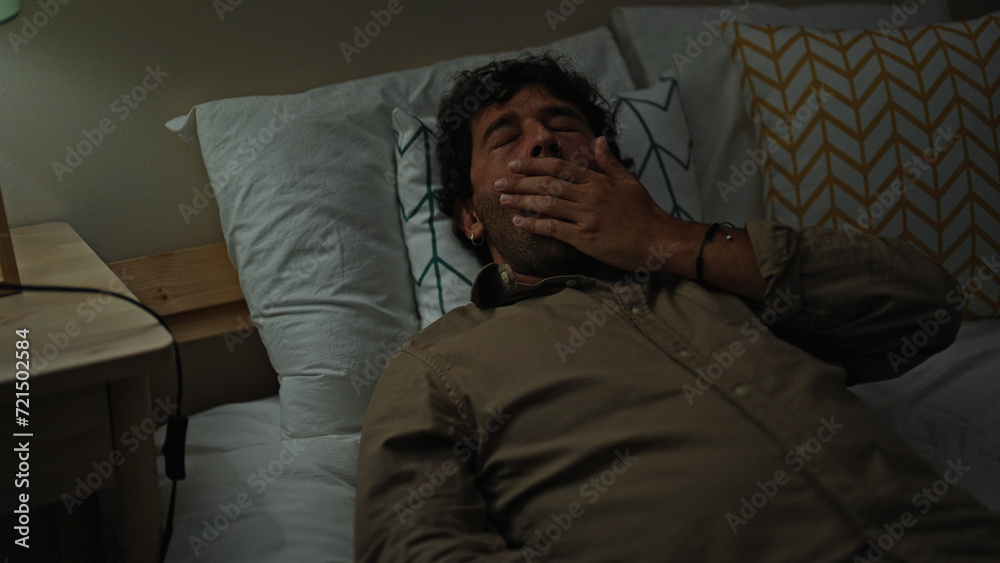Young hispanic man lying on bed tired yawning at bedroom Young hispanic man lying on bed tired yawning at bedroom