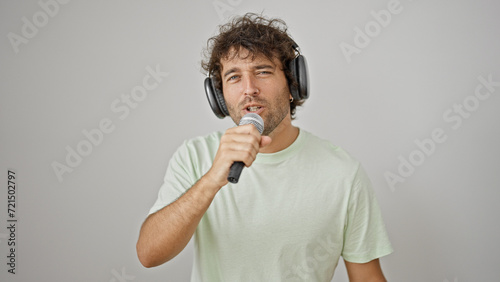 Young hispanic man listening to music singing song over isolated white background