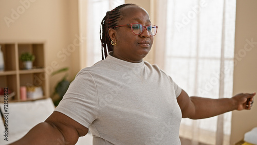 Plus size african american woman meditating, taking deep breaths in cosy bedroom, awake and looking calm under morning blanket