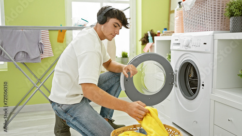 Handsome young hispanic teenager rocks out, engrossed in music, while tackling laundry chores in the household's wash room