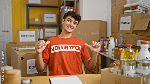 Young hispanic teenager pointing to volunteer uniform smiling at charity center