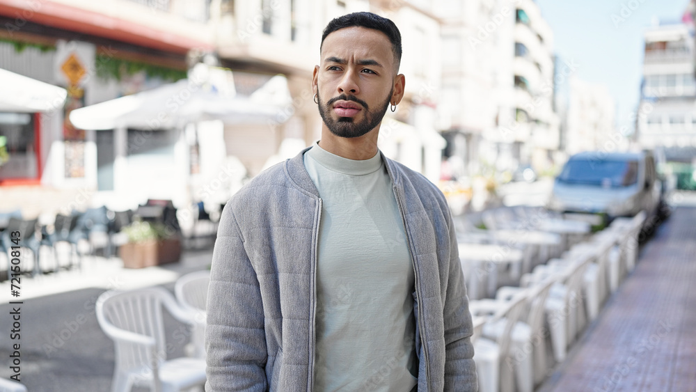 Young hispanic man standing with serious expression at street Young hispanic man standing with serious expression at street