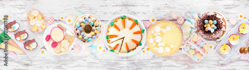 Easter or spring dessert food table scene. Top view over a white wood banner background. Lemon tart, cupcakes, Easter egg and carrot cakes and an assortment of sweets.