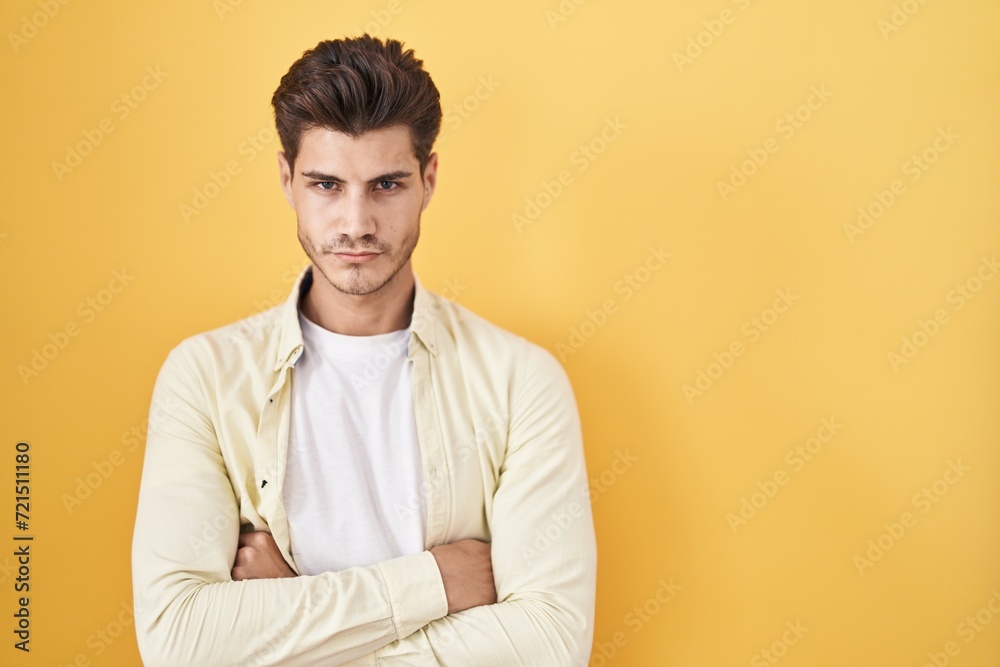 Young hispanic man standing over yellow background skeptic and nervous, disapproving expression on face with crossed arms. negative person. Young hispanic man standing over yellow background skeptic and nervous, disapproving expression on face with crossed arms. negative person.