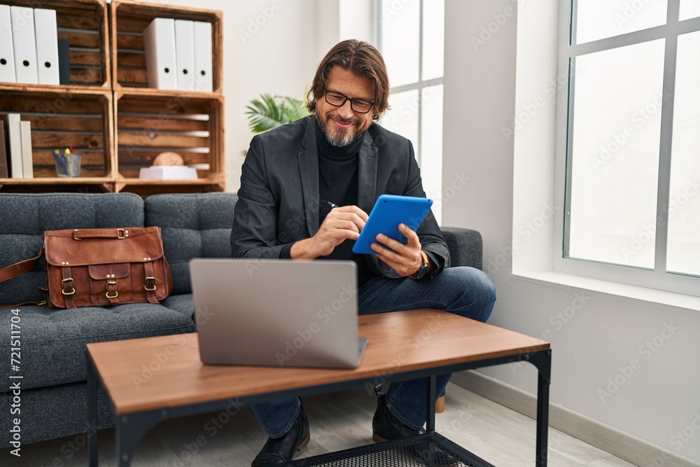 Middle age man psychologist using laptop and touchpad at psychology clinic Middle age man psychologist using laptop and touchpad at psychology clinic