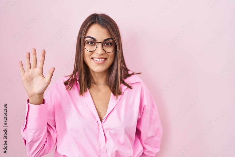 Young hispanic woman wearing glasses standing over pink background showing and pointing up with fingers number five while smiling confident and happy. Young hispanic woman wearing glasses standing over pink background showing and pointing up with fingers number five while smiling confident and happy.