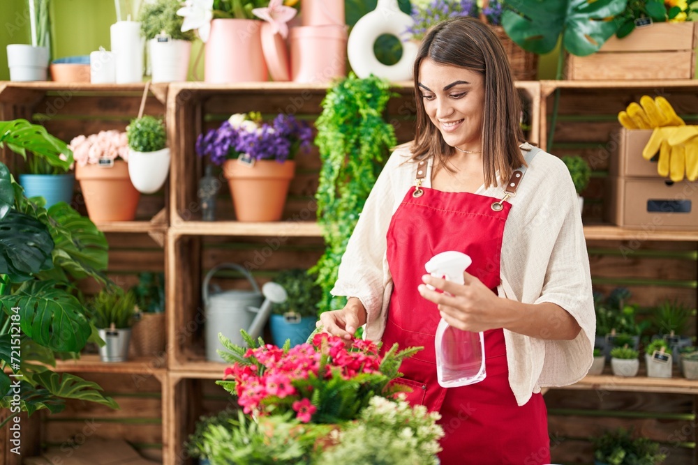 Young beautiful hispanic woman florist using diffuser watering plant at flower shop