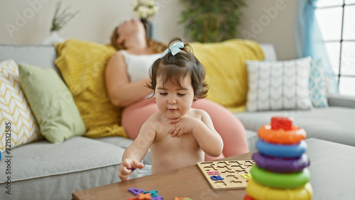 Exhausted mother and mum's lovely baby play together, as the older daughter enjoys a much-needed relaxing rest on the comfy living room sofa at home, embodying pure casual family lifestyle.