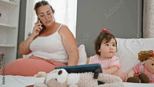 Heartwarming family moment, mother and daughter sitting on bed together, talking heart to heart on smartphone, while navigating touchpad