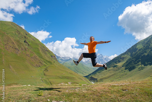 Adrenaline Rush: A Man in an Orange T-Shirt Jumps against Green Mountains