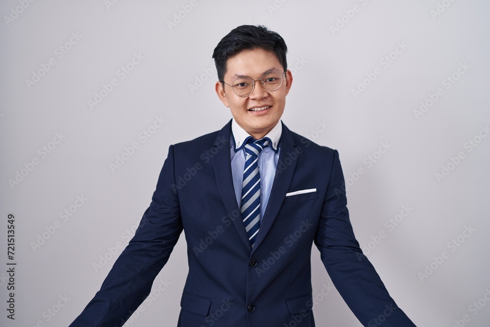 Young asian man wearing business suit and tie smiling cheerful with open arms as friendly welcome, positive and confident greetings Young asian man wearing business suit and tie smiling cheerful with open arms as friendly welcome, positive and confident greetings