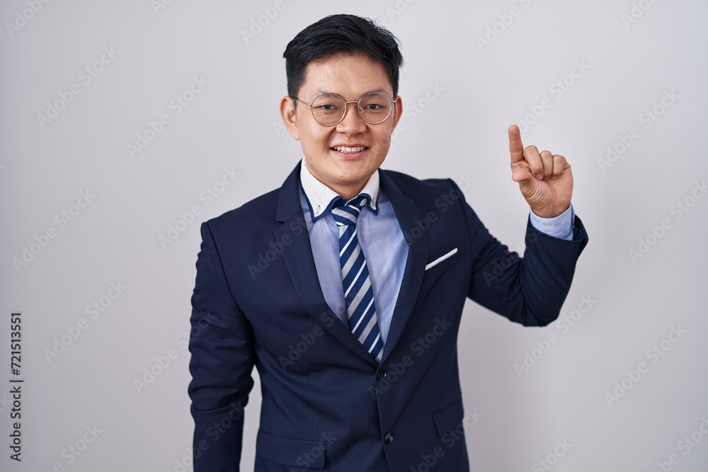 Young asian man wearing business suit and tie smiling and confident gesturing with hand doing small size sign with fingers looking and the camera. measure concept. Young asian man wearing business suit and tie smiling and confident gesturing with hand doing small size sign with fingers looking and the camera. measure concept.