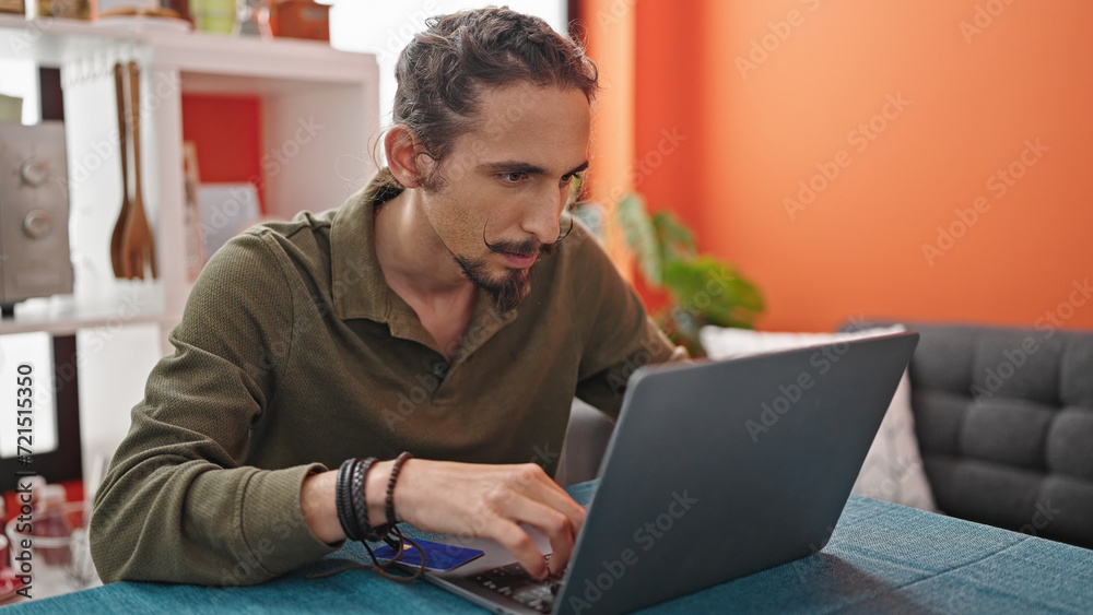 Young hispanic man using laptop sitting on table at dinning room