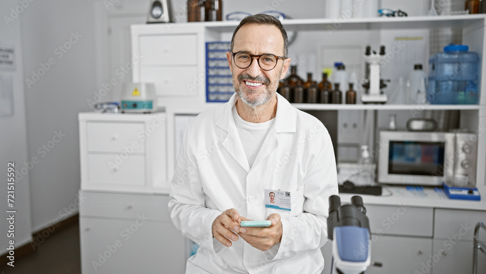 Grey-haired middle age man, brimming with confidence, happily utilizing his smartphone for medical research in the heart of a bustling science lab Grey-haired middle age man, brimming with confidence, happily utilizing his smartphone for medical research in the heart of a bustling science lab