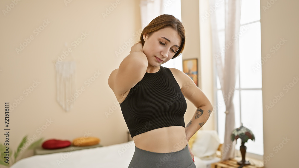 Young brunette woman experiencing neck pain in a cozy bedroom setting, depicting health and wellness within a home environment.