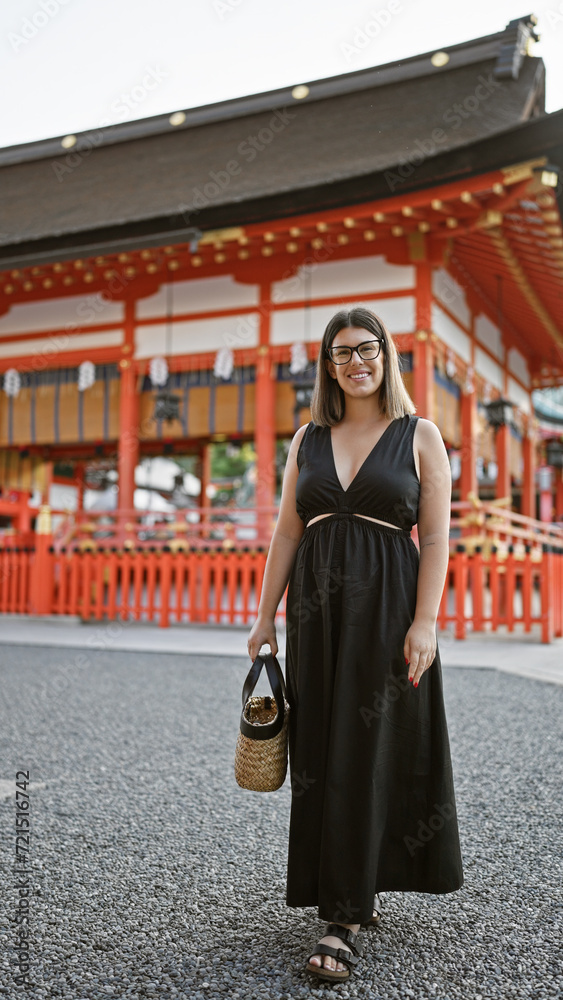 Captivating glimpse of a joyful confident hispanic woman, flashing a beaming smile in glasses, casually posing and walking towards the camera at the iconic fushimi inari-taisha in kyoto, japan.