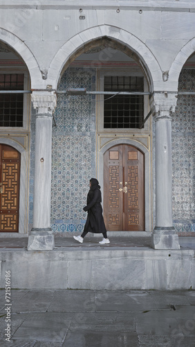 A woman in black strolls past the intricate tilework of istanbul's topkapi palace, exemplifying cultural exploration.