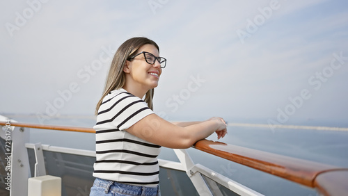 Smiling woman in glasses enjoying her vacation on a cruise ship deck with a vast ocean and clear sky in the background.