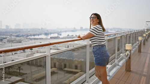 Smiling woman enjoying a cruise vacation, standing on the ship deck overlooking the sea. © Krakenimages.com