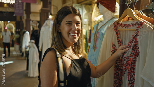 Canvas Print A smiling young woman shops for traditional clothing at a souk in dubai, exuding the charm of an arabian tourist destination