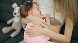 Mother and daughter sitting on sofa breastfeeding baby at home