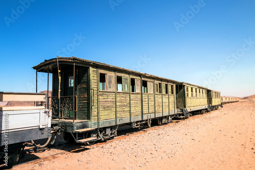 An old green wooden railcar from a bygone era rests on the tracks in a wild and sunny desert environment