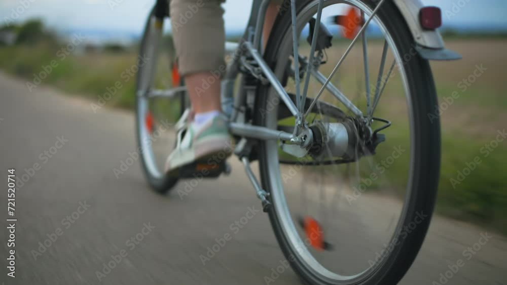 ecological transport, a young woman pedals a bicycle while riding along a road among a field, wheel close-up ecological transport, a young woman pedals a bicycle while riding along a road among a field, wheel close-up