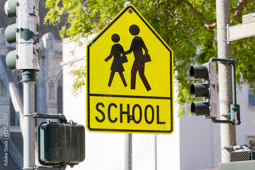 Yellow warning road sign for a school zone at a road intersection with a street traffic light in the background. Yellow School Zone Street Sign, Close-up. School Road Sign with Children, Foreground photo