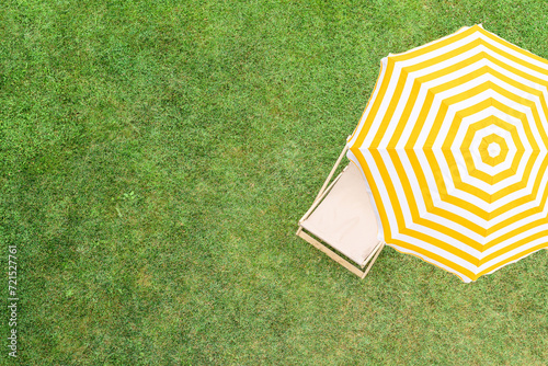 Yellow umbrella with deck chair on the green grass sunbathes at summer day. Top view, drone, aerial view. © flowertiare