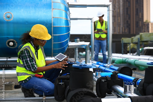 Diversity engineers wearing reflect green  safety vests and helmet  working to checking Industry cooling systems, and HVAC of large industrial building 