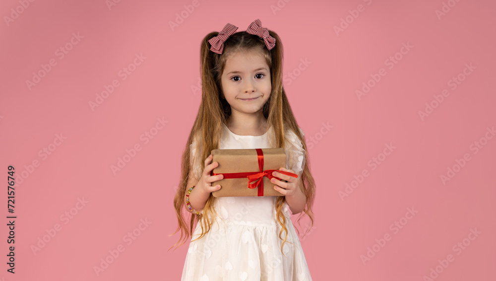 A little girl dressed in a prom dress with two very beautiful pigtails in her hair with two attractive pink bows. She is holding a gift she received for the holidays.