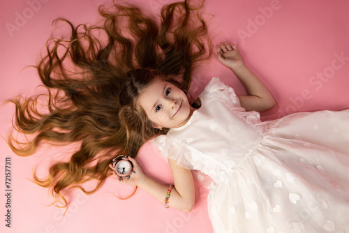 A beautiful little girl in a very attractive white dress, lying on a pink background with her hair very well arranged and very beautiful and attractive, the little girl has simple hair and takes care