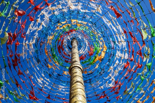 Vibrant Tibetan prayer flags form a captivating circular display around a central pole against a clear blue sky in Qinghai's historic Amdo region.