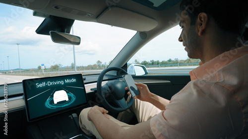 Self driving car or autonomous vehicle travel on speed highway with driverless system and autopilot mode allowing man driver relax and focus on smartphone without compromising safety. Perpetual photo