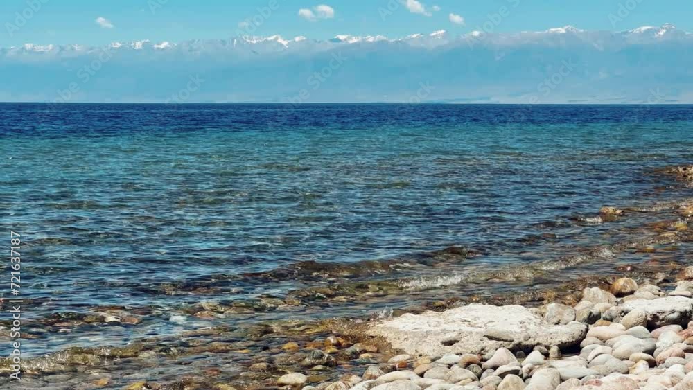 View of Issyk-Kul mountain lake, Kyrgyzstan. Waves splash on a sandy beach with rocks. Calm, peaceful natural background. Lake with a view of the Tien Shan Mountains. Kyrgyzstan 4K View of Issyk-Kul mountain lake, Kyrgyzstan. Waves splash on a sandy beach with rocks. Calm, peaceful natural background. Lake with a view of the Tien Shan Mountains. Kyrgyzstan 4K