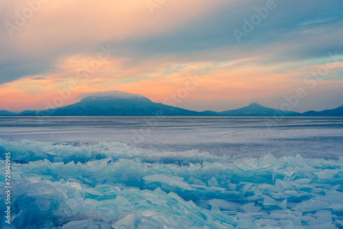 Fonyod, Hungary - Beautiful icebergs on the shore of the frozen Balaton. Badacsony and Gulacs with a spectacular cloudy sunset in the background. Winter landscape. photo