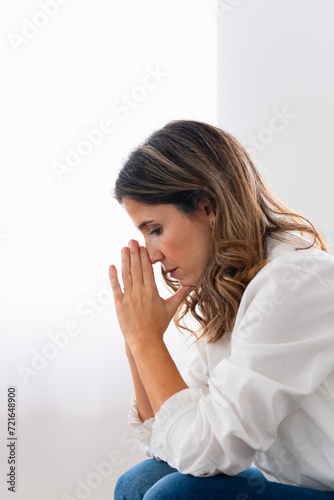 Vertical side view of a pensive and sad woman sitting alone at home