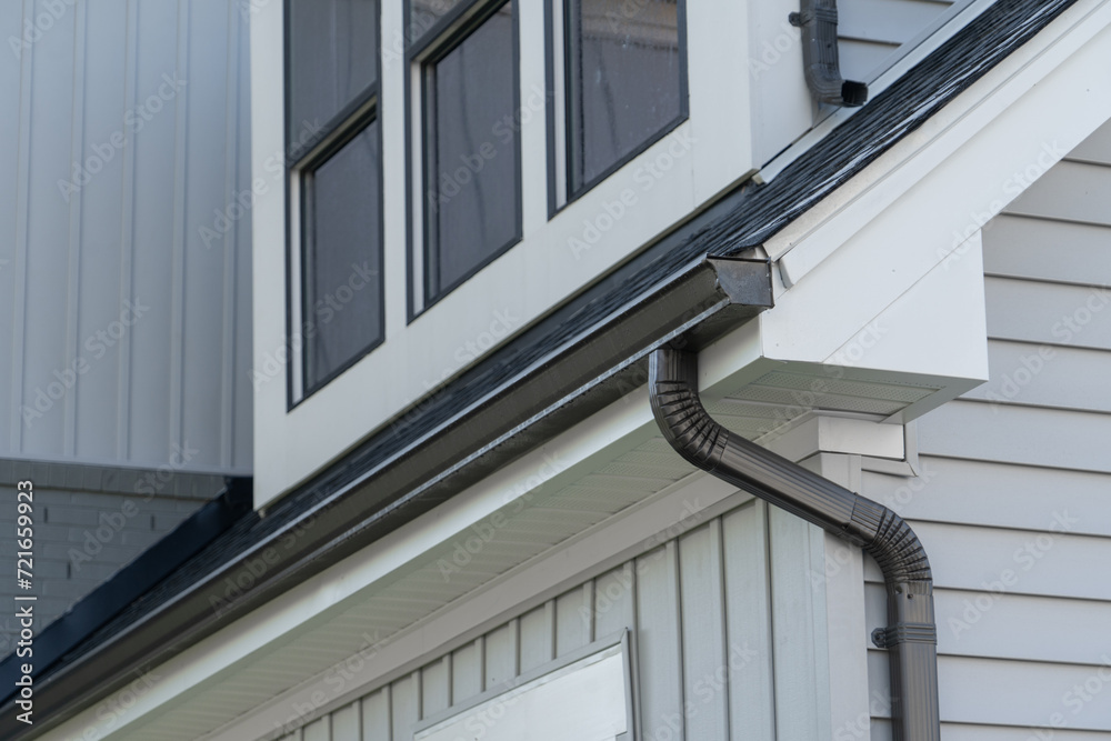 Dark brown frame gutter guard system, with white horizontal and vertical vinyl siding fascia, drip edge, soffit, on a pitched roof attic at a luxury American single family