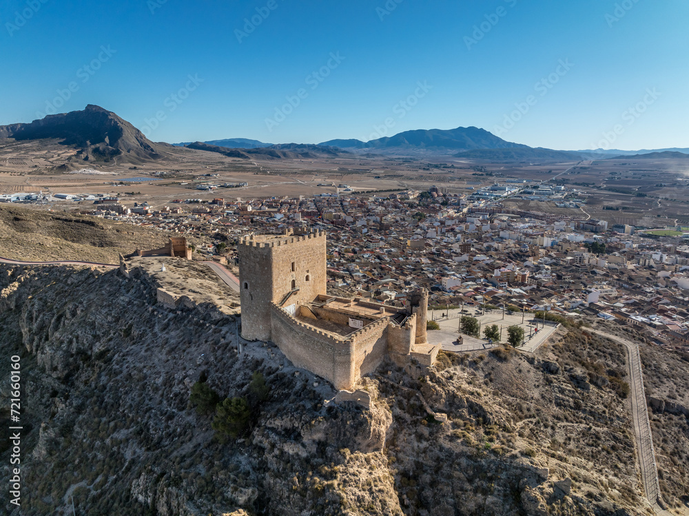 Obraz premium Aerial view of Jumilla medieval castle in Murcia Spain, on a hilltop, imposing irregular shape keep with four floors, crenelated battlements cloudy blue sky background