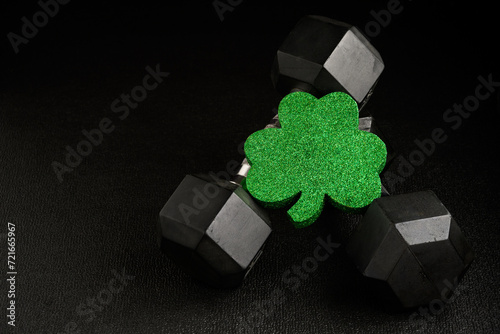 Holiday fitness and Happy St. Patick’s Day, green glitter shamrock shape with a pair of dumbbells on a black background
 photo