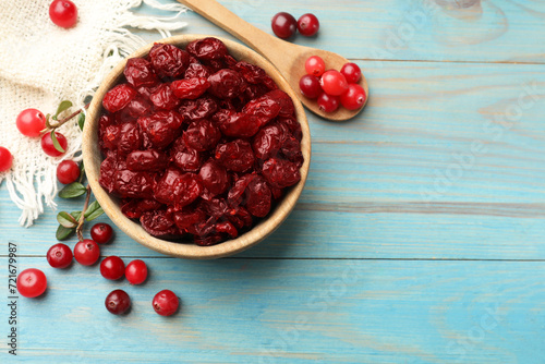 Tasty dried cranberries in bowl and fresh ones on light blue wooden table, top view. Space for text