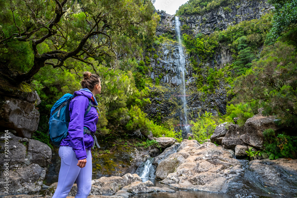 Low angle shot of female tourist with backpack enjoing the natural atmosphere at high waterfall. Lagoa do Vento waterfall, Madeira Island, Portugal, Europe.