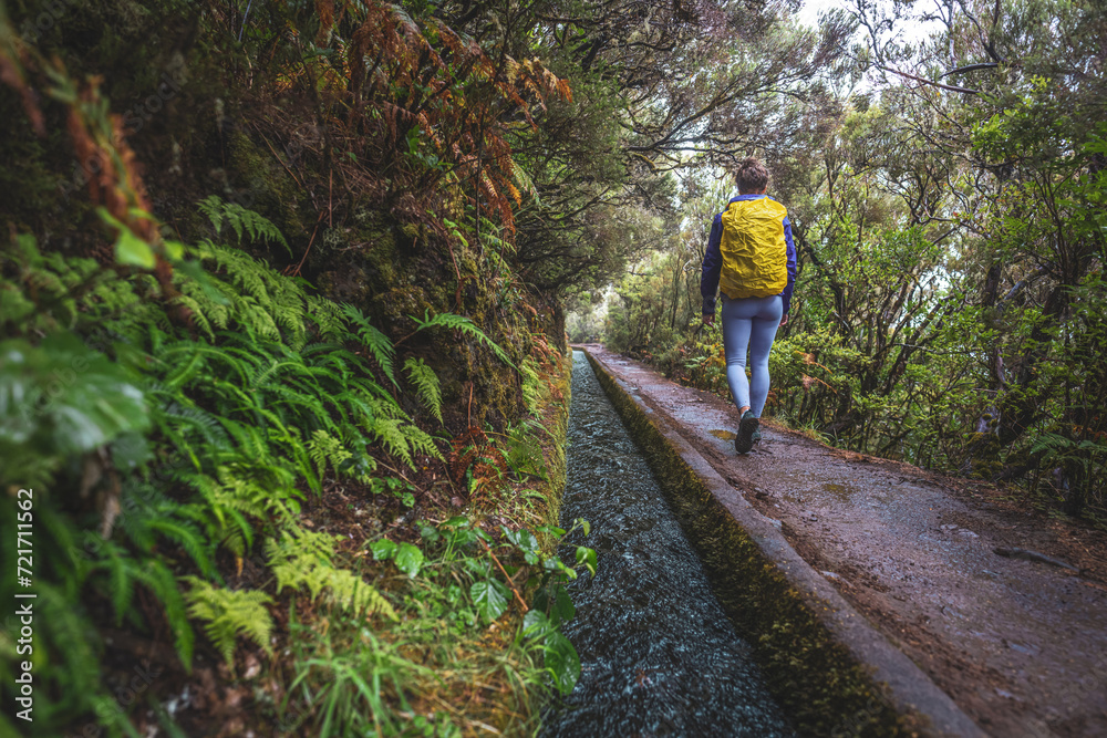 Female tourist with backpack walks along water channel path through a laural forest on a rainy day. 25 Fontes waterfalls, Madeira Island, Portugal, Europe.