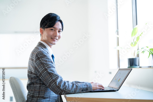 オフィスでパソコン作業をするジャケットを着た若い男性