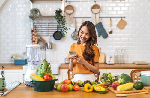 Portrait happy beauty slim healthy asian woman use phone and vegan food healthy fresh vegetable and fruit in kitchen.diet  vegetarian  eating  fruit  wellness  health  green food.Fitness  healthy food